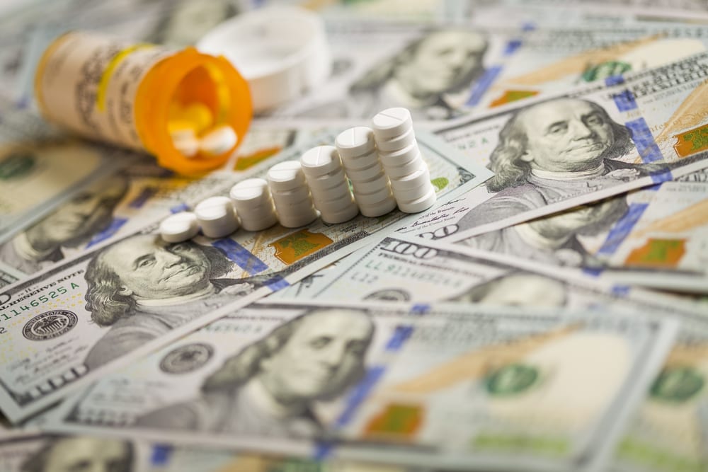 [prescription pills in a rising bar graph on $100 bills]